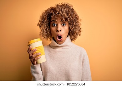 Young african american curly woman drinking cup of takeaway coffee over yellow background scared in shock with a surprise face, afraid and excited with fear expression