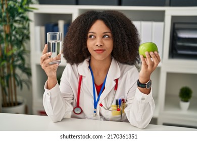 Young African American Dietitian Woman Holding Fresh Apple And Water Smiling Looking To The Side And Staring Away Thinking. 