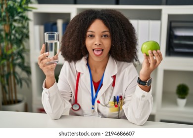 Young African American Dietitian Woman Holding Fresh Apple And Water Sticking Tongue Out Happy With Funny Expression. 