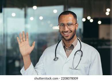 Young African American Doctor Man Wearing Glasses Wearing Medical Coat Saying Hello Happy And Smiling Friendly Welcoming Gesture Doctor Working Inside Clinic