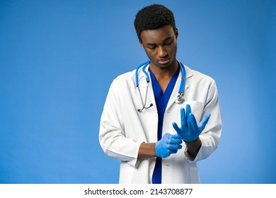 Young African American doctor putting on surgical gloves on blue background - Powered by Shutterstock