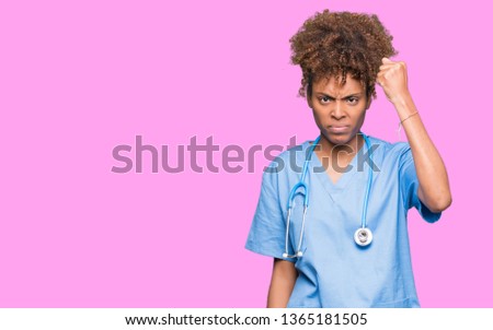 Young african american doctor woman over isolated background angry and mad raising fist frustrated and furious while shouting with anger. Rage and aggressive concept.