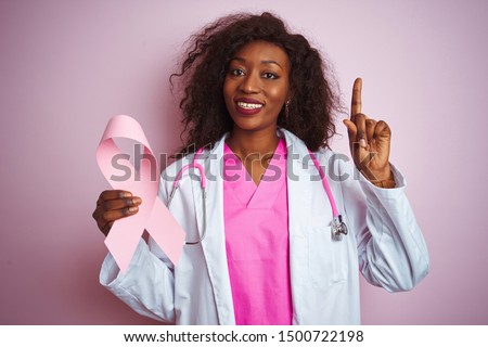 Young african american doctor woman holding cancer ribbon over isolated pink background surprised with an idea or question pointing finger with happy face, number one