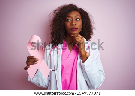 Young african american doctor woman holding cancer ribbon over isolated pink background serious face thinking about question, very confused idea