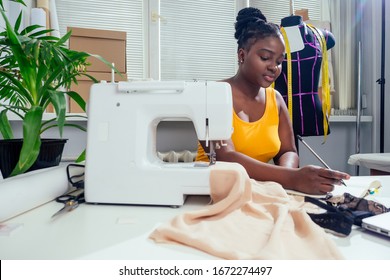 Young african american dressmaker woman sews clothes on sewing machine at tailor office it tropical summer style