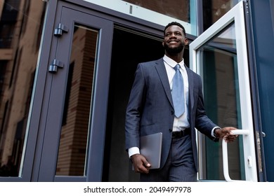Young African American Entrepreneur Man Leaving Business Center Building After Work, Looking Away And Smiling, Copy Space. Business People And Successful Career Concept