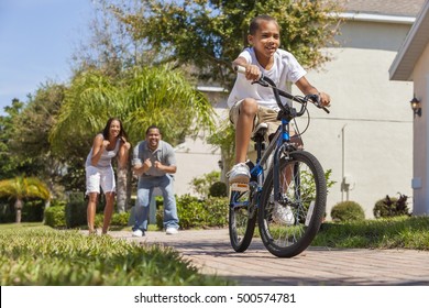 A Young African American Family With Boy Child Riding His Bicycle And His Happy Excited Parents Giving Encouragement Behind Him