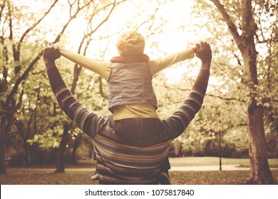 Young African American Father Carrying His Daughter On Shoulders. From Back.