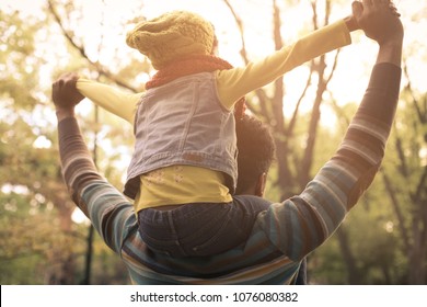 Young African American Father Carrying His Daughter On Shoulders. From Back.