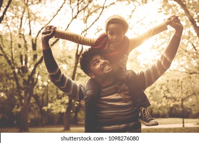 Young African American Father Carrying Daughter On Shoulders.