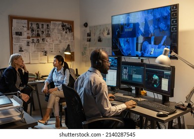 Young African American FBI agent sitting in front of computer monitors and screen in office while watching security camera records