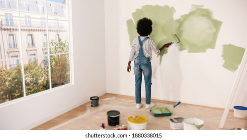 Young African American Female Alone Painting Wall With Roller Brush In Olive Color While Renovating Apartment. Rear Of Woman Redecorating Home, Renovating And Improving Repair And Decorating Concept