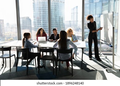 Young African American female coach or speaker make flip chart presentation to diverse businesspeople at meeting in office. Woman tutor or trainer present project on whiteboard to diverse colleagues. - Powered by Shutterstock