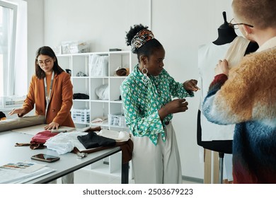 Young African American female fashion designer and her male colleague standing in front of mannequin and creating new attire - Powered by Shutterstock