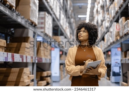 Young African American female looking at camera working in warehouse using digital tablet checking inspection on shelves.woman worker check stock inspecting in storage logistic factory.