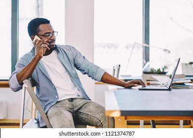 Jeune freelance afro-américaine discutant sur son téléphone portable assis sur son bureau, un branleur à la peau noire appelant au logiciel de mise à jour du service d'assistance à la clientèle pour travailler sur un ordinateur portable