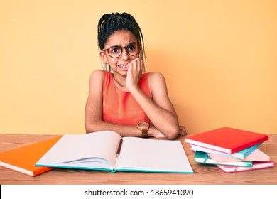 Young african american girl child with braids studying for school exam looking stressed and nervous with hands on mouth biting nails. anxiety problem. 