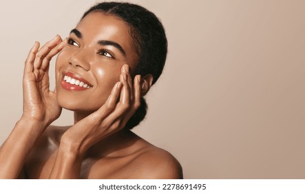 Young african american girl with clear, glowing facial skin, washes her face with cosmetic product, smiling and looking up, enjoys smooth feeling after hydrating serum, face mask - Powered by Shutterstock