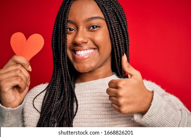 Young African American Girl Holding Romantic Heart Paper Shape Over Red Isolated Background Happy With Big Smile Doing Ok Sign, Thumb Up With Fingers, Excellent Sign