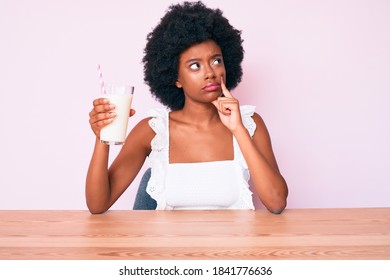 Young African American Girl Holding Glass Of Milk Serious Face Thinking About Question With Hand On Chin, Thoughtful About Confusing Idea 