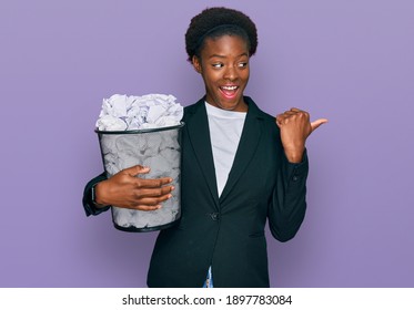 Young African American Girl Holding Paper Bin Full Of Crumpled Papers Pointing Thumb Up To The Side Smiling Happy With Open Mouth 