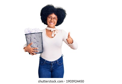 Young African American Girl Holding Paper Bin Full Of Crumpled Papers Smiling Happy And Positive, Thumb Up Doing Excellent And Approval Sign 