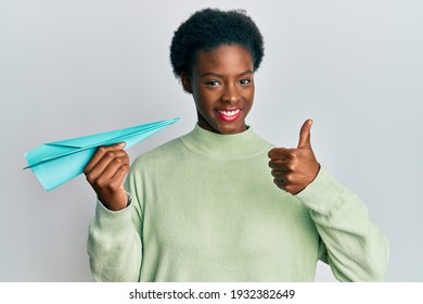 Young African American Girl Holding Paper Airplane Smiling Happy And Positive, Thumb Up Doing Excellent And Approval Sign 