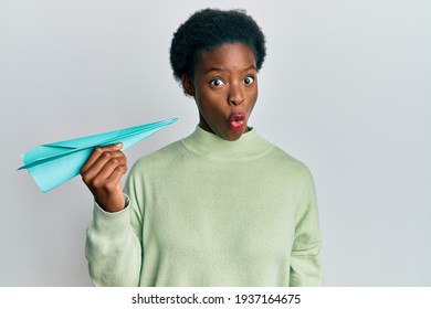 Young African American Girl Holding Paper Airplane Scared And Amazed With Open Mouth For Surprise, Disbelief Face 