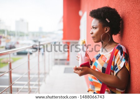 Young african american girl holding burger in her hands outdoor and posing for camera.