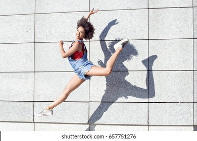 Young african american girl jumping,smiling. Outdoor photo.