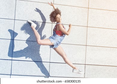 Young african american girl jumping,smiling. Outdoor photo.