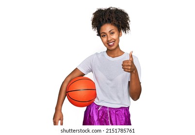Young african american girl playing baseball holding bat and ball smiling happy and positive, thumb up doing excellent and approval sign 