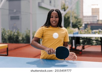 Young African American girl practices her table tennis skills, hitting the ball with a focused expression as she enjoys a game on a sunny day. Sport concept - Powered by Shutterstock