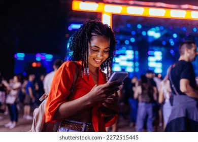 A young African American girl is with a smartphone at a music festival, texting with her friends. - Shutterstock ID 2272515445