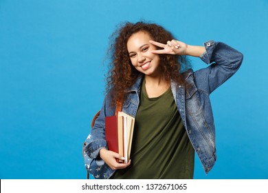 Young african american girl teen student in denim clothes, backpack hold books isolated on blue background studio portrait. Education in high school university college concept. Mock up copy space