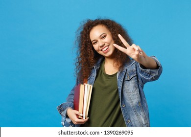 Young african american girl teen student in denim clothes, backpack hold books isolated on blue background studio portrait. Education in high school university college concept. Mock up copy space