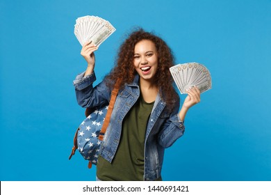 Young african american girl teen student in denim clothes, backpack hold money isolated on blue background studio portrait. Education in high school university college concept. Mock up copy space