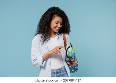 Young African American Girl Teen Geography Student Wear Denim Clothes Backpack Spin Choose Country Earth World Globe Isolated On Blue Background Education In High School University College Concept.