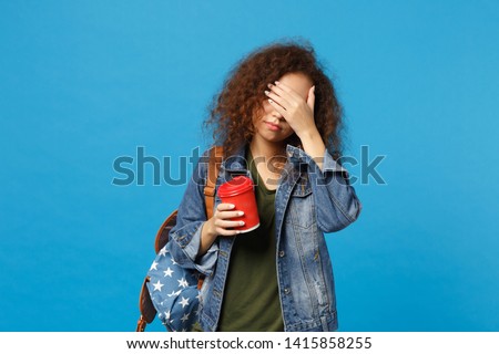 Young african american girl teen student in denim clothes, backpack hold paper cup isolated on blue background studio portrait. Education in high school university college concept. Mock up copy space