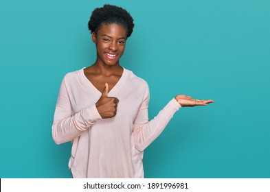 Young african american girl wearing casual clothes showing palm hand and doing ok gesture with thumbs up, smiling happy and cheerful 