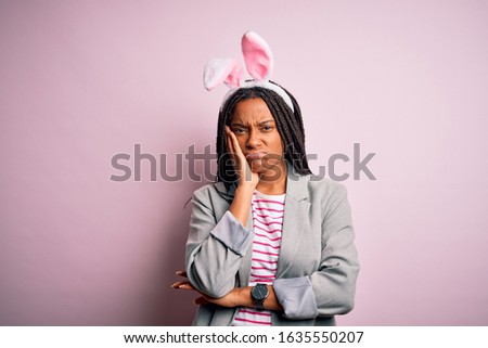 Young african american girl wearing cute easter bunny ears over pink background thinking looking tired and bored with depression problems with crossed arms.