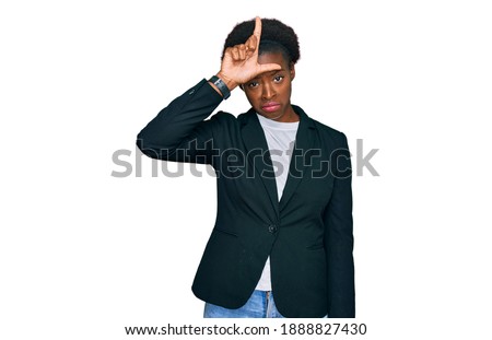 Young african american girl wearing business clothes making fun of people with fingers on forehead doing loser gesture mocking and insulting. 