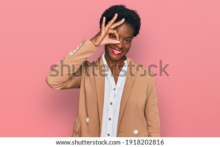 Young african american girl wearing business clothes smiling happy doing ok sign with hand on eye looking through fingers 