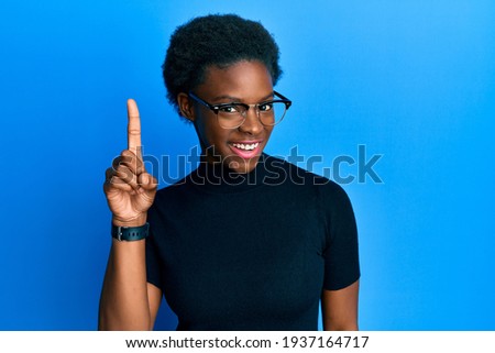 Young african american girl wearing casual clothes and glasses smiling with an idea or question pointing finger up with happy face, number one 
