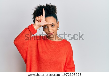 Young african american girl wearing casual clothes making fun of people with fingers on forehead doing loser gesture mocking and insulting. 