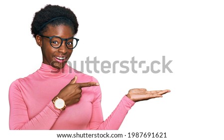 Young african american girl wearing casual clothes and glasses amazed and smiling to the camera while presenting with hand and pointing with finger. 