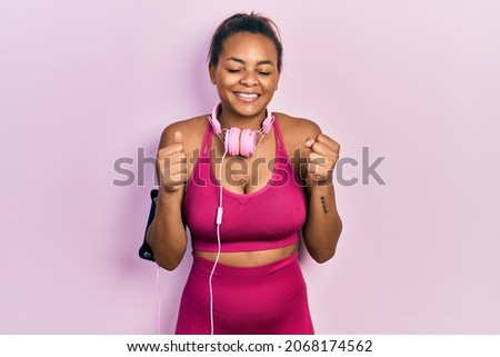 Young african american girl wearing gym clothes and using headphones excited for success with arms raised and eyes closed celebrating victory smiling. winner concept. 