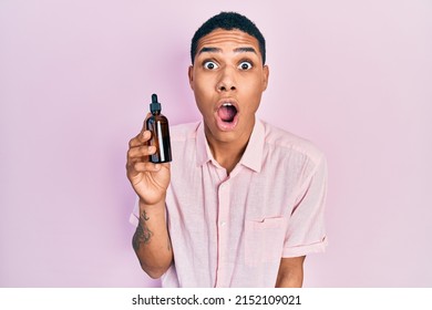 Young African American Guy Holding Serum Bottle Scared And Amazed With Open Mouth For Surprise, Disbelief Face 