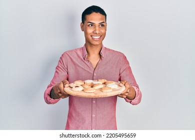 Young African American Guy Holding Tray With Cake Sweets Smiling Looking To The Side And Staring Away Thinking. 