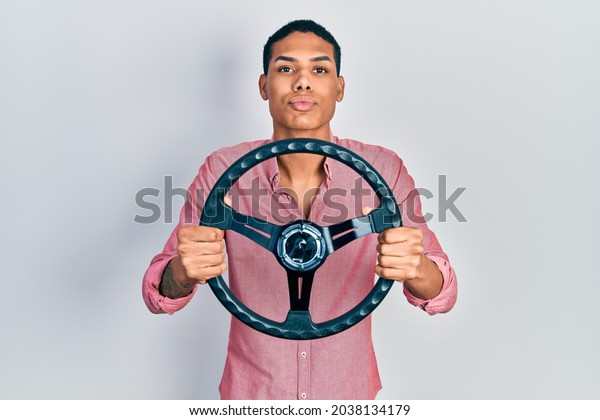 Young african american guy holding steering wheel\
looking at the camera blowing a kiss being lovely and sexy. love\
expression. 